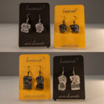 Hängende Ohrringe mit Karl-Marx-Kopf Motiv aus Epoxidharz, in Varianten mit und ohne Sockel, präsentiert auf gelben und schwarzen Karten.