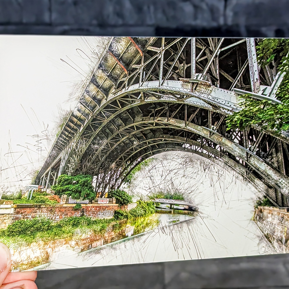 Künstlerisch gestaltete Postkarte mit dem Viadukt in Chemnitz, in einem feinen Aquarell- und Zeichenstil dargestellt. Man sieht die geschwungenen Stahlbögen und viel Grün; das Motiv wird von einer Hand vor einer grauen Steinwand gehalten.
